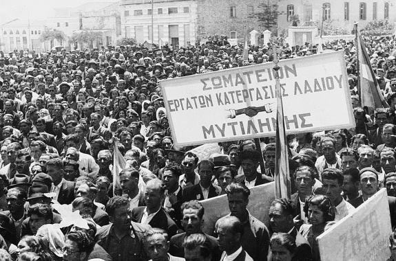 Εργατική Πρωτομαγιά 1945 στο σημερινό Δημοτικό Πάρκο Αγίας Ειρήνης Μυτιλήνης. Απέναντι φαίνονται οι τότε Αποθήκες Πετρόπουλου (μετέπειτα κινηματογράφος «ΑΡΙΩΝ») και η σημερινή Δημόσια Κεντρική Βιβλιοθήκη Μυτιλήνης στην οδό Σμύρνης (Αρχείο λεσβιακής εφημερίδας «Νέο Εμπρός»). 